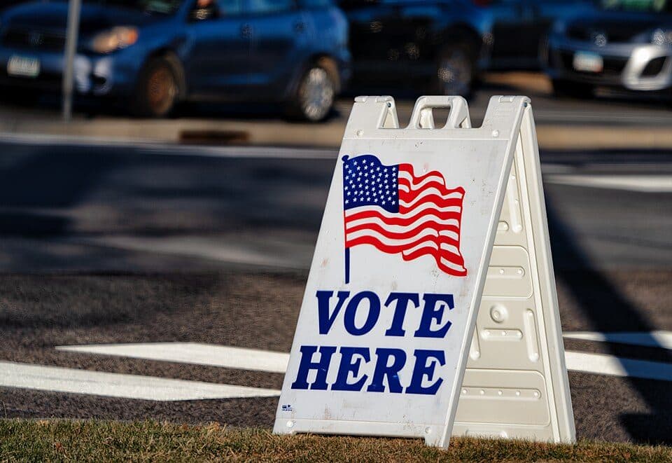 A Vote Here sign with an American flag outside a polling place